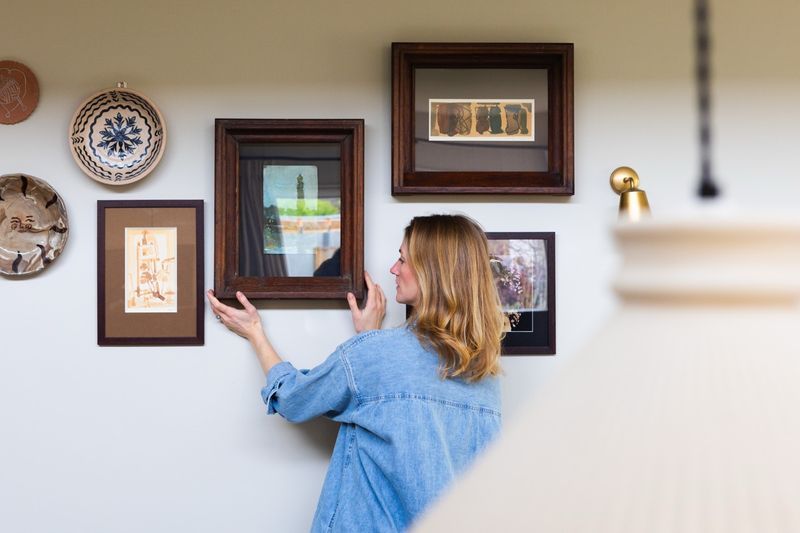 Emily arranging a collection of framed vintage and antique art